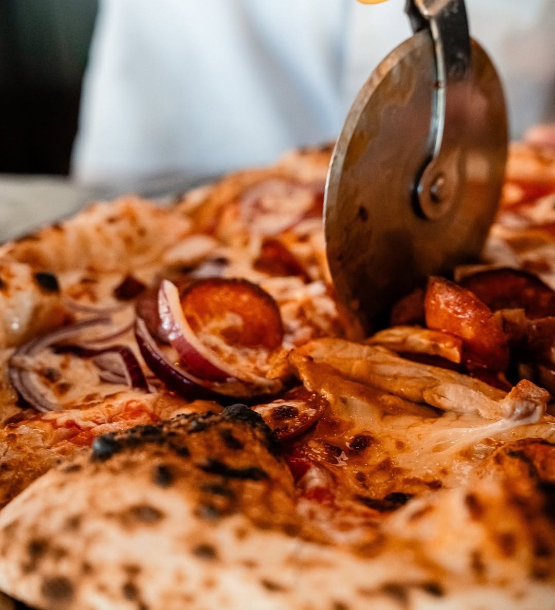 Pizza com pepperoni e cebola roxa a ser cortada com um corta-pizzas